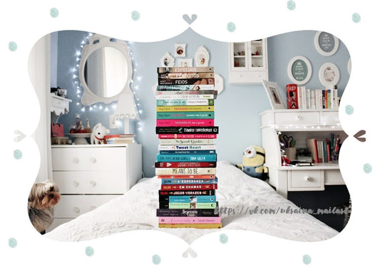 Hoher Bücherstapel auf einem Bett mit einem kleinen Yorkshire Terrier auf dem Boden eines hellblauen Zimmers