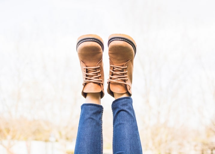 Legs in jeans and tan boots kicked up against a pale autumn sky