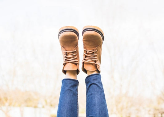 Legs in jeans and tan boots kicked up against a pale autumn sky