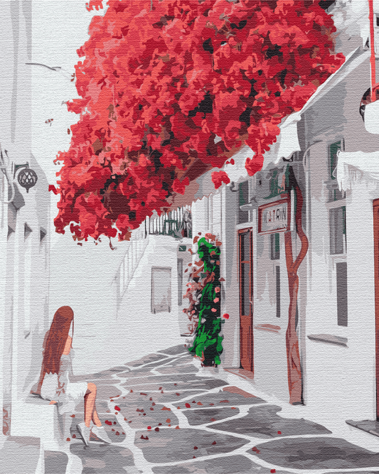 Girl sitting beneath a cascade of red bougainvillea in a white Greek island alley