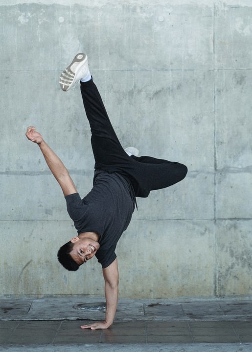 Breakdancer im Freeze auf einer Hand, Turnschuh hoch in der Luft vor einer Betonwand