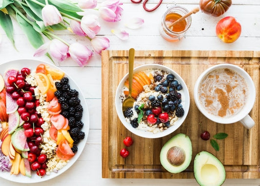 Smoothie-Bowl, frisches Obst, Avocado und rosa Tulpen auf einem Holztisch arrangiert