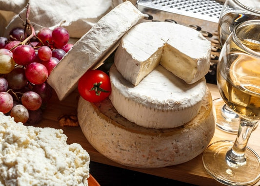 Sliced brie wheel with grapes, cherry tomato, and wine glasses on a wooden board