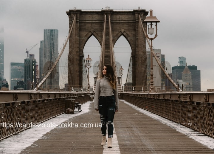 Frau im grauen Pullover geht an einem verschneiten Wintermorgen über die Brooklyn Bridge