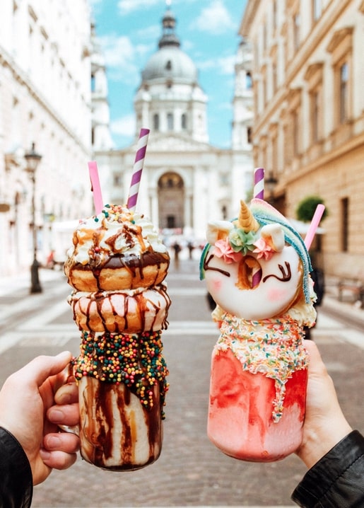 Zwei Hände mit Milchshakes voller Donuts vor der Stephansbasilika in Budapest