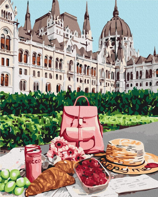 Picnic with croissants, raspberries and a straw hat set before the Hungarian Parliament building