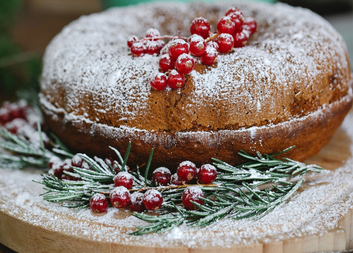 Powdered bundt cake with red currants and rosemary on a wooden board