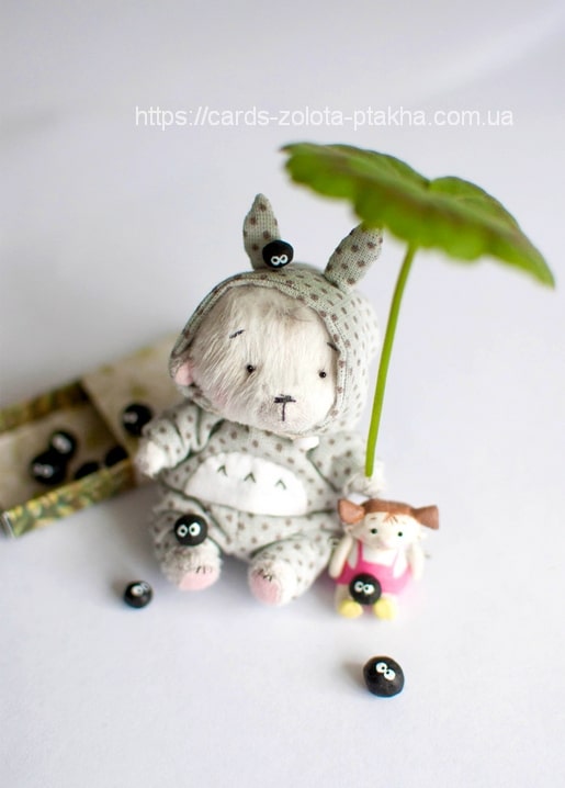 Cream mohair bunny in a hooded outfit under a leaf umbrella beside a small doll and black soot-sprites