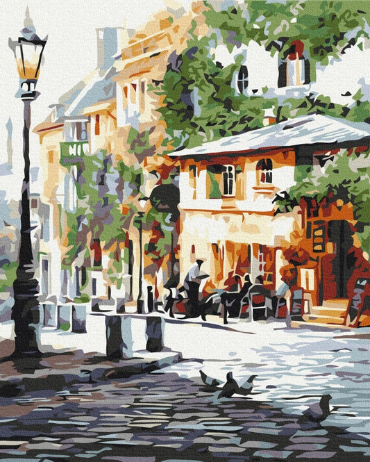 Illustrated street corner with a lamppost, café terrace under trees, and pigeons on cobblestones