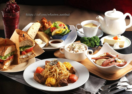 Café table spread with sandwiches, pasta, salad, rice, sausages, cheesecake and a teapot