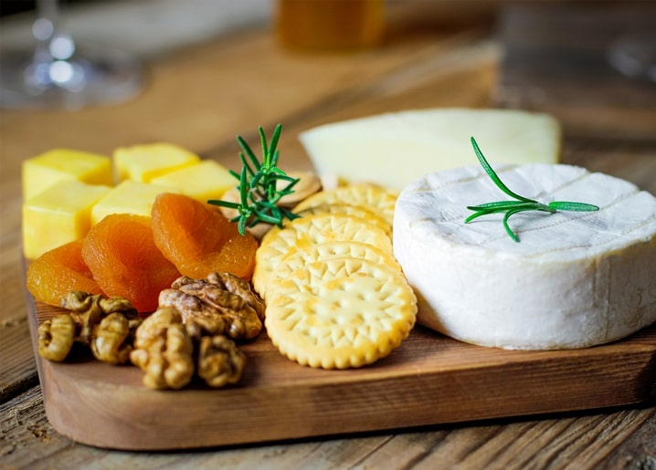 Camembert wheel with rosemary beside dried apricots, walnuts, and crackers on a wooden board
