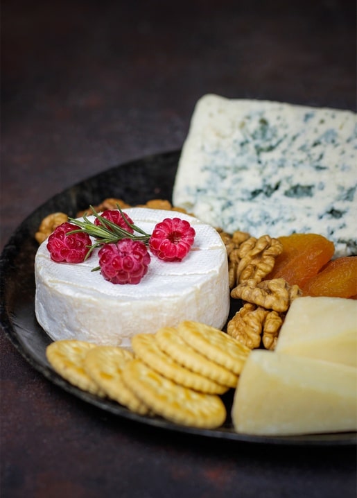 Camembert mit Himbeeren und Rosmarin neben Blauschimmelkäse, Crackern und Walnüssen