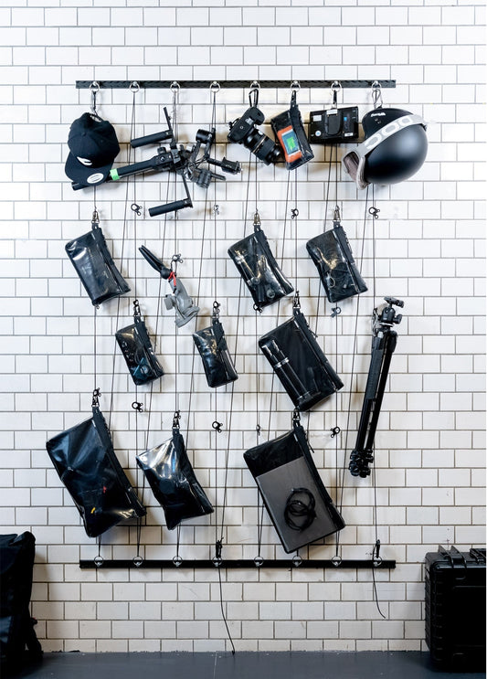 Kameras, Helm und schwarze Taschen hängen an einer Schiene