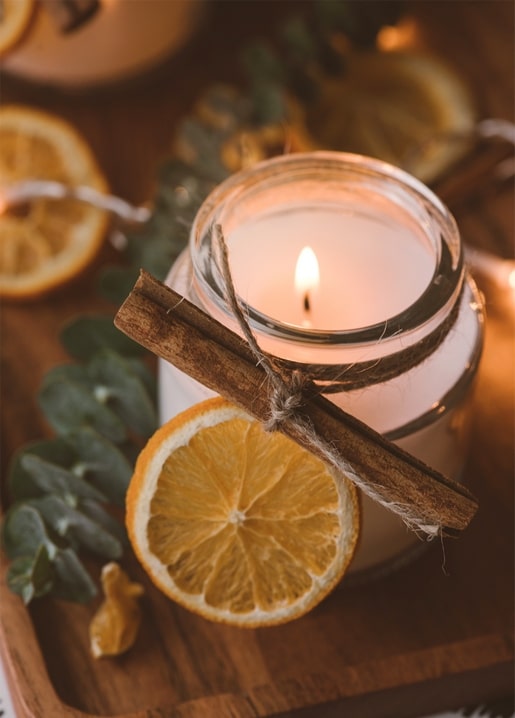 Brennende Kerze im Glas mit Zimtstange neben getrockneten Orangenscheiben und Eukalyptus