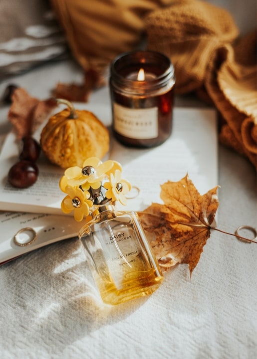 Lit candle, floral-capped perfume bottle, mini pumpkin, and maple leaf on an open book