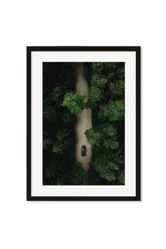 Aerial photography poster of a dark car on a dirt road through dense forest