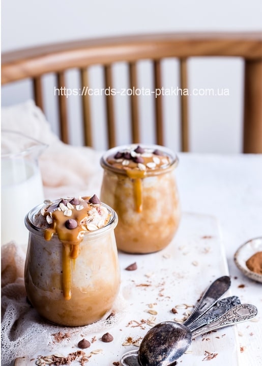 Zwei Gläser Overnight Oats mit Karamell und Schokostückchen neben einem Glas Milch und Löffeln.