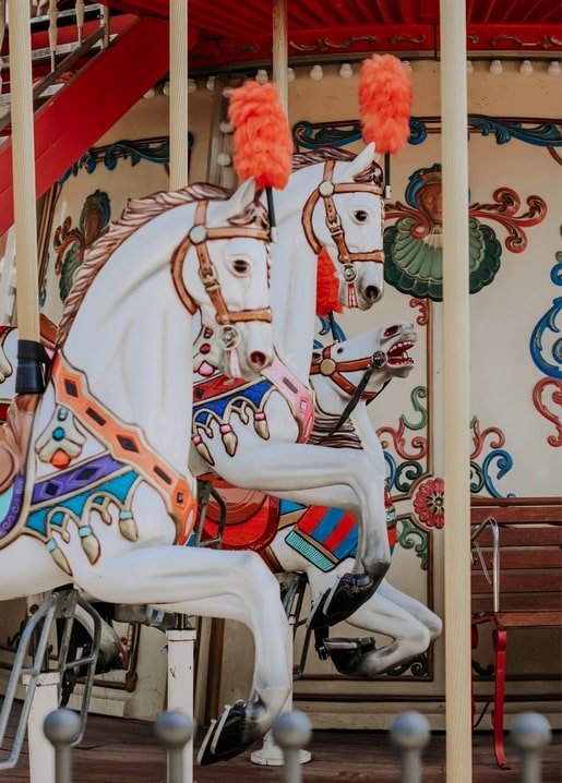 Hand-painted carousel horses mid-gallop, one with a bright orange plume, on a vintage fairground ride