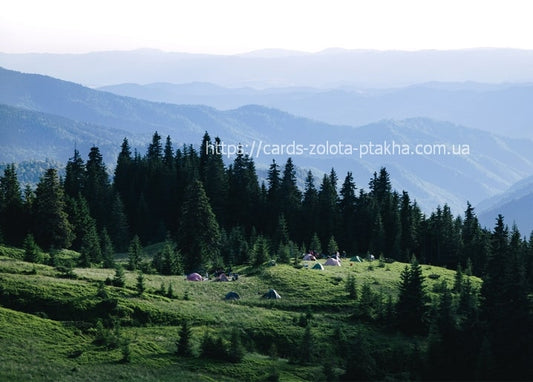 Tents pitched in a green mountain meadow with misty Carpathian ridges beyond
