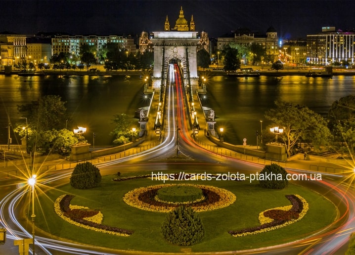 Chain Bridge illuminated at night in Budapest with St. Stephen's Basilica dome behind