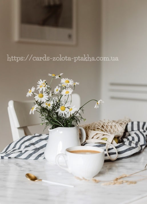 Weißer Krug mit Kamillenblüten neben einer Kaffeetasse auf einem Marmortisch