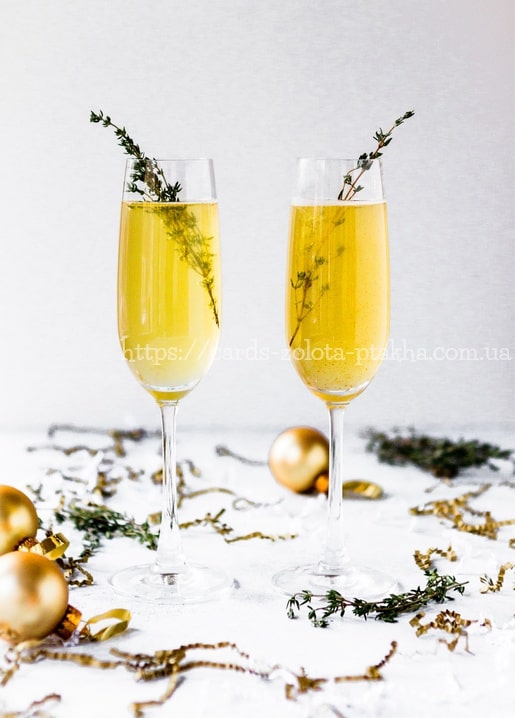Zwei Sektgläser mit Rosmarinzweigen zwischen goldenen Kugeln und Konfetti