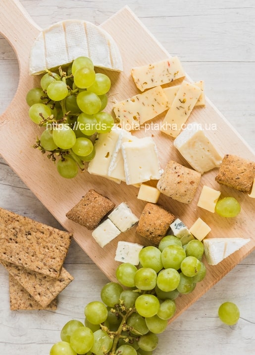 Holzbrett mit Camembert, Käsewürfeln, Crackern und grünen Trauben