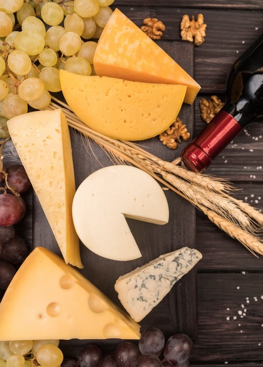 Käseplatte mit Trauben, Walnüssen, Weizenähren und Rotwein