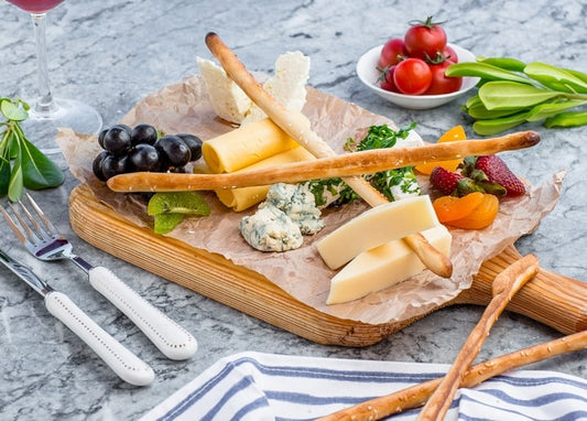 Käsebrett mit Grissini, Blauschimmelkäse, Weintrauben, Erdbeeren und einem Glas Rotwein