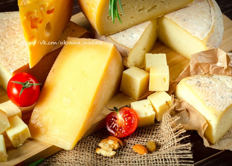 Cubes of Swiss and yellow cheese with walnuts, almonds, and a halved cherry tomato on burlap
