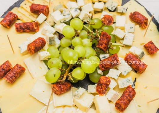 Cheese platter with brie, blue cheese, grapes and chorizo bites on slate