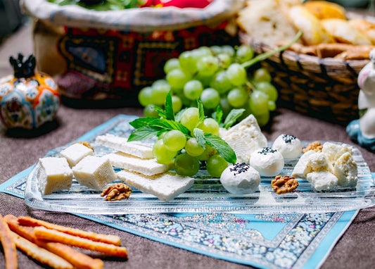 Weicher Käse, grüne Weintrauben und Minze auf einem gemusterten Tablett mit Brotkorb