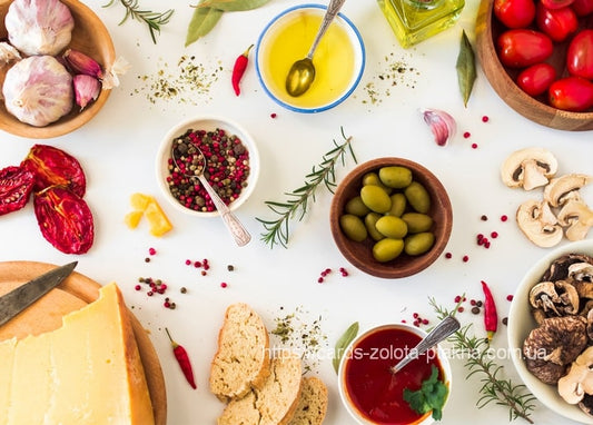 Cheese, olives, cherry tomatoes, bread, mushrooms and rosemary arranged on a white table.