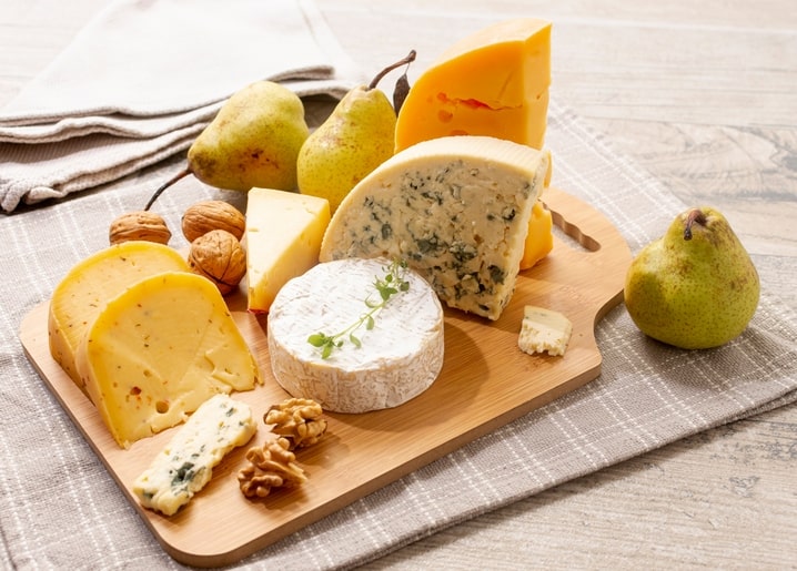 Wooden board with blue cheese, cheddar and brie, ripe pears and cracked walnuts on linen cloth