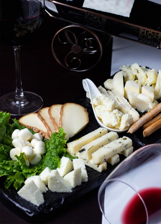 Käseplatte mit Mozzarella, Brotstangen und Salat neben einem Glas Rotwein