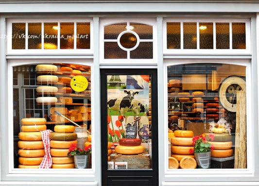 Cheese shop window with stacked wheels of Gouda, a cow poster, and red tulips in pots