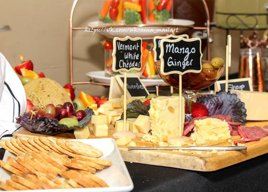 Cheese tasting board with Vermont cheddar and mango ginger labels, crackers, grapes, and salami