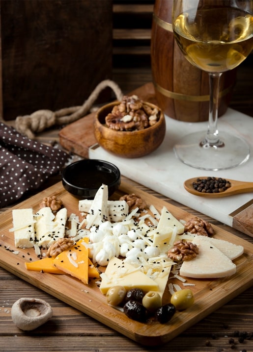 Holzbrett mit Käse, Walnüssen, Oliven, Pfeffer und einem Glas Weißwein