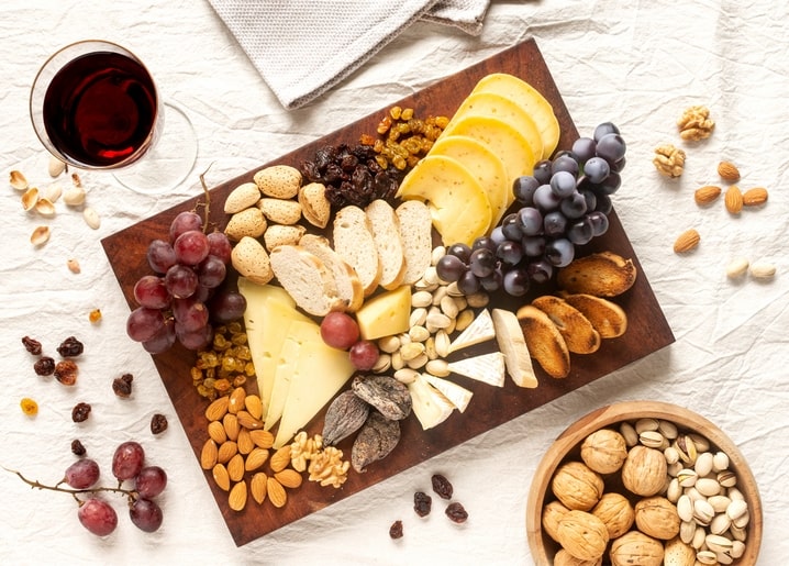 Wooden board with cheese, grapes, walnuts, almonds, dried figs, bread and a glass of red wine