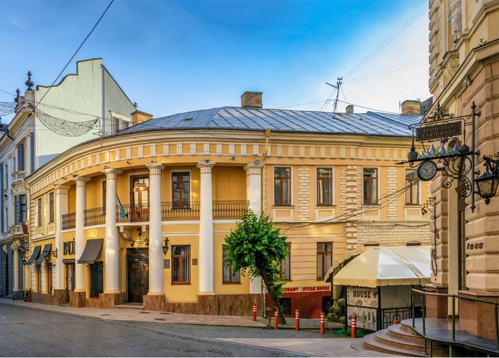 Yellow curved corner building with a white colonnade on a cobblestone street in Chernivtsi