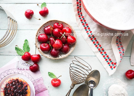 Schale Kirschen, Stück Kirschkuchen, Schneebesen und besticktes Tuch auf Holztisch