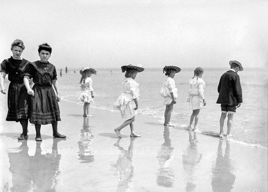 Schwarz-weiß Foto von Kindern mit Sonnenhüten am Strand entlang des Ufers