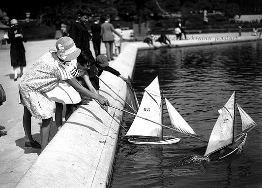 Schwarz-weißes Foto von Kindern, die Segelboote auf einem Parkteich steuern
