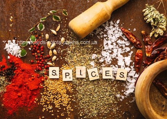 Dried chili peppers, paprika, salt and herbs around a wooden mortar, with wooden letters spelling SPICES.