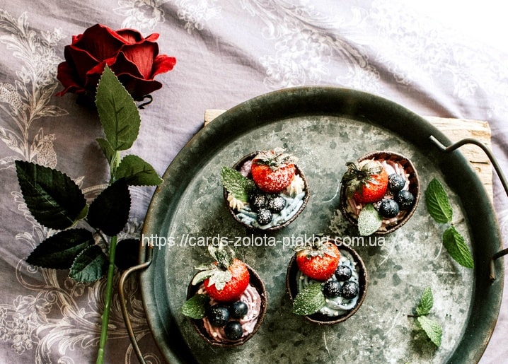 Schokoladen-Tartelettes mit Erdbeeren und Blaubeeren auf einem Tablett, daneben eine rote Rose