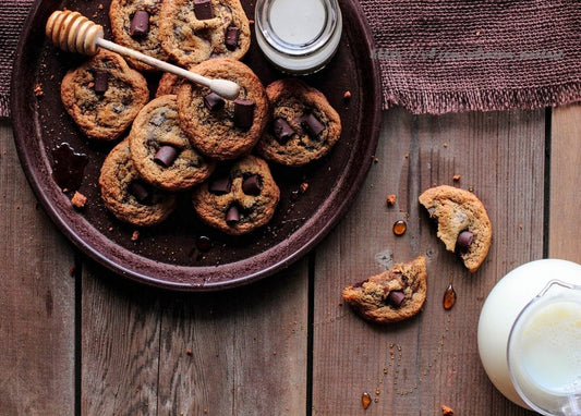 Stapel Schokoladenkekse mit Honiglöffel und Milchkännchen auf Holztisch