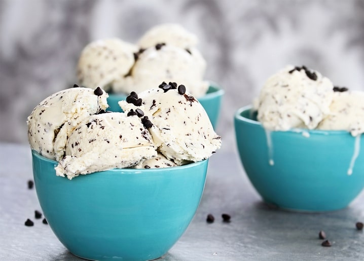 Scoops of chocolate-chip ice cream piled in turquoise bowls with chips scattered on marble