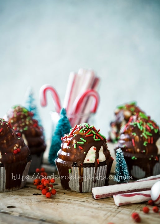 Schokoladen-Cupcakes mit Zuckerstangen und kleinen Weihnachtsbäumen auf einem Holztisch