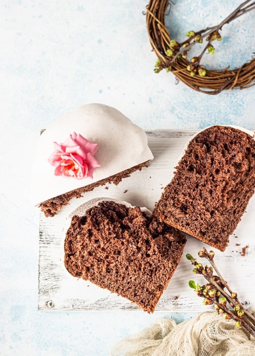 Sliced chocolate Easter bread with white icing and a pink rose beside a twig wreath