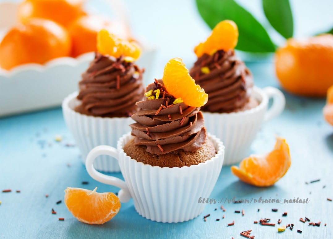 Schokoladen-Cupcakes mit Mandarinenspalten in Mini-Teetassen auf hellblauem Untergrund